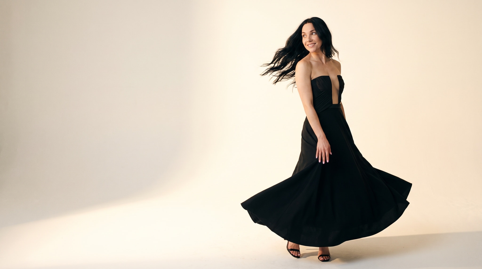 The house model turning mid-step in a black gown, hair in motion, photographed by Shoppermo in a bright minimal studio.